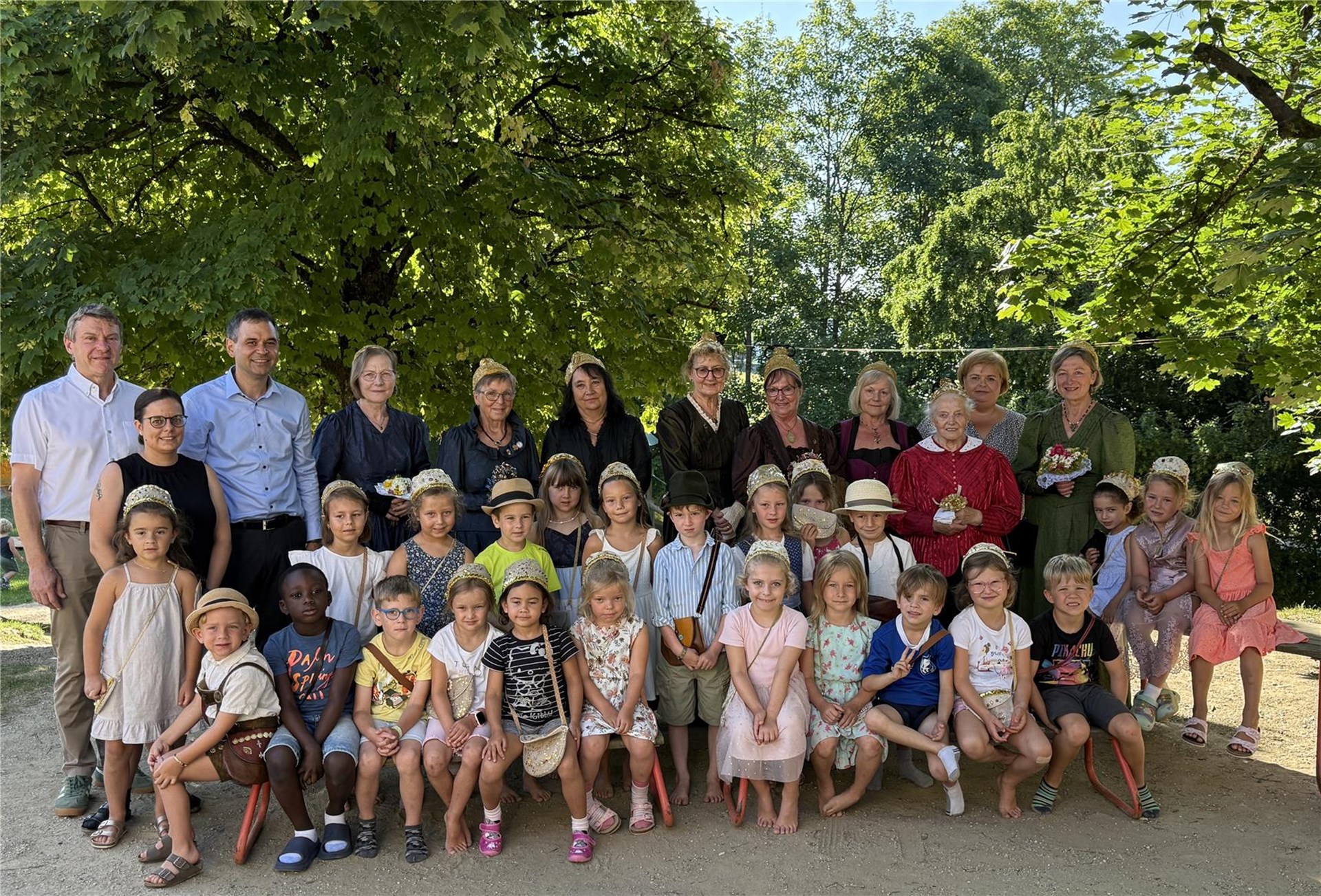 Kinder und Erwachsene stehen im Garten des Kindergartens Büchlberg und präsentieren selbstgemachte Goldhauben.